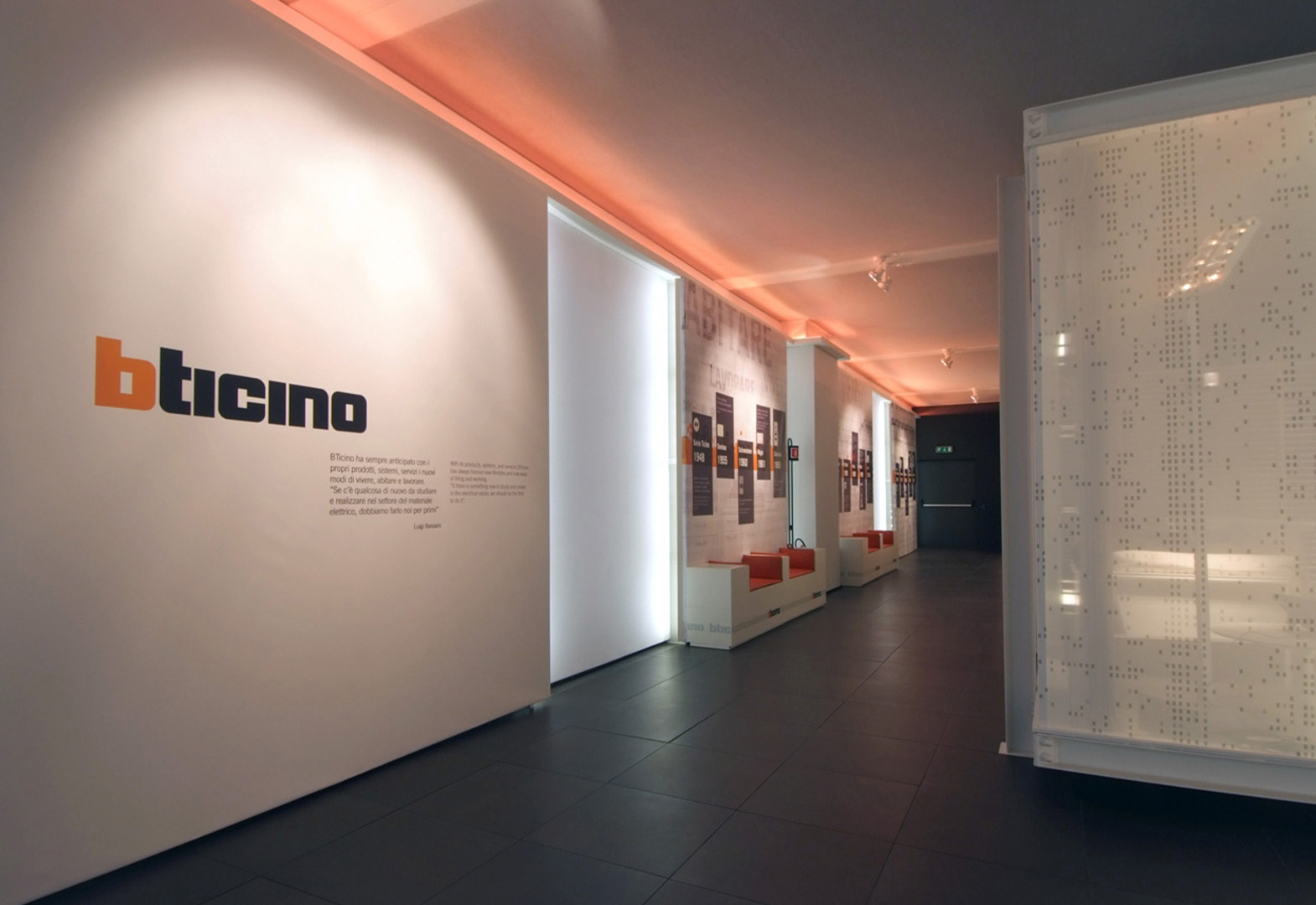 Corridoio moderno all'interno della sede BTicino, con branding, plafoniere arancioni e display informativi.